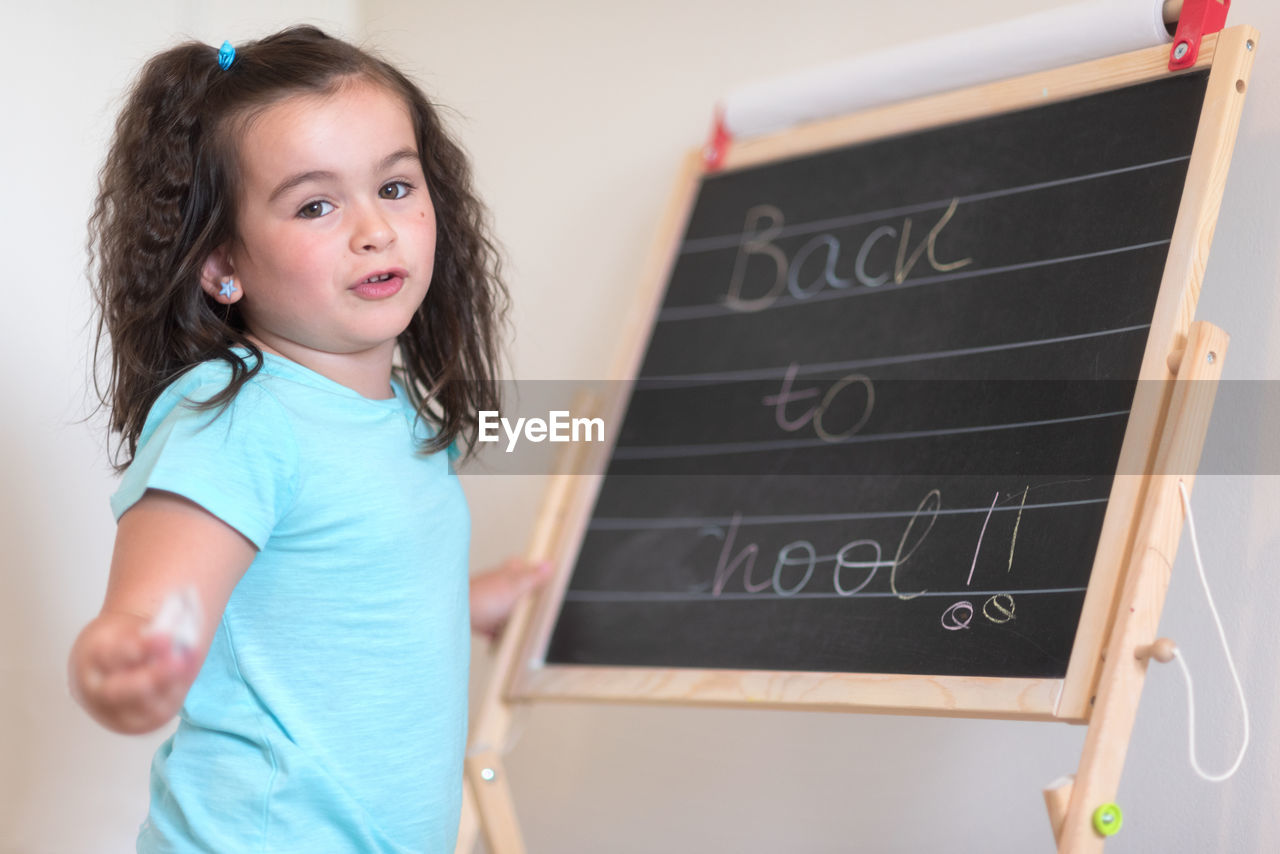 Portrait of smiling girl rubbing text from blackboard in classroom
