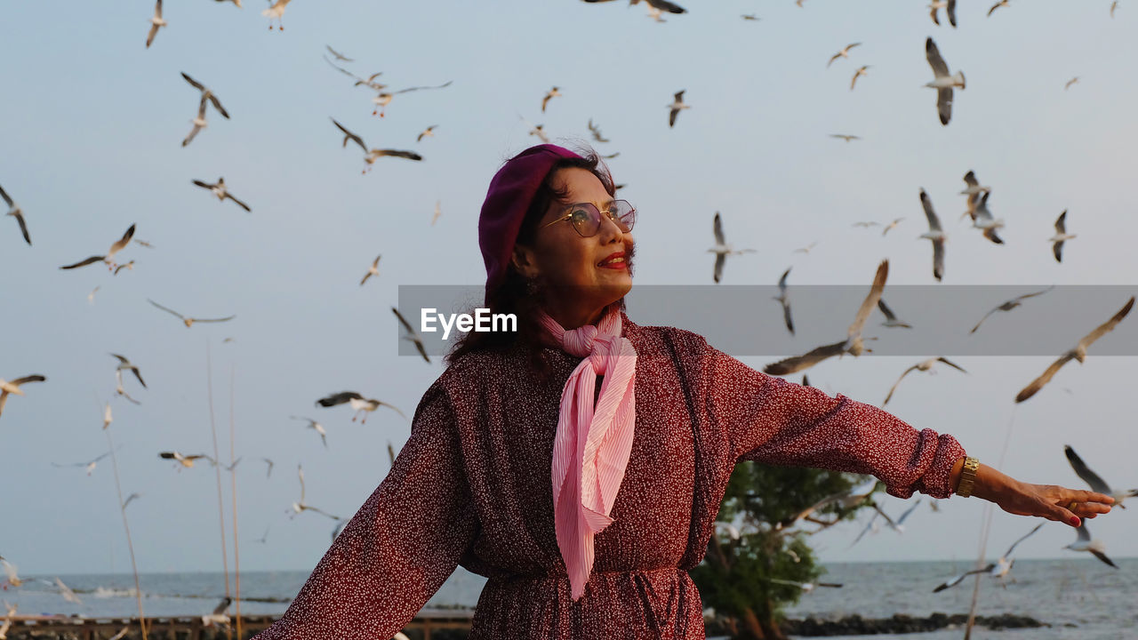 Woman standing with seagulls flying in background at beach