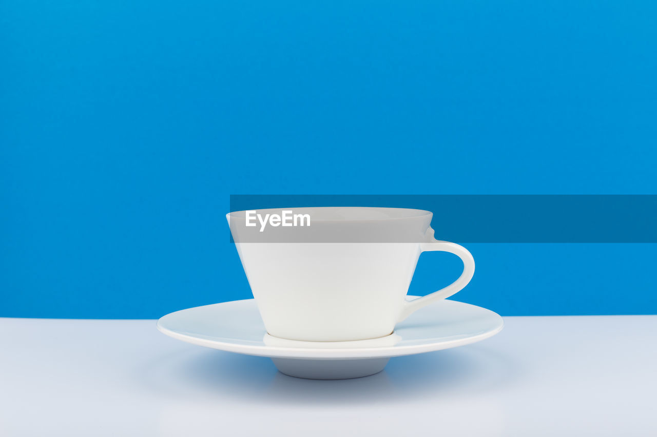 White ceramic coffee cup on a white table with blue background