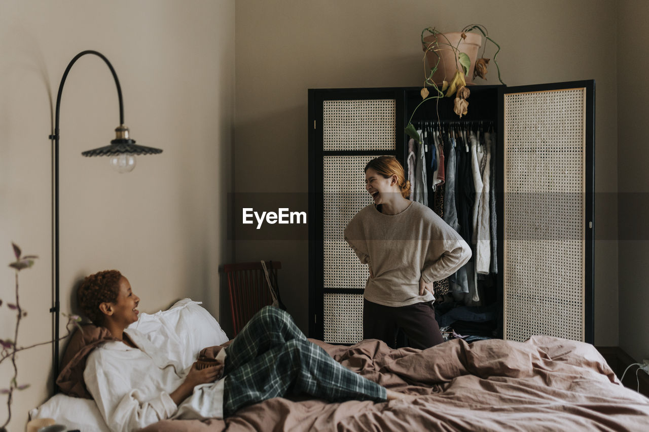 Non-binary couple laughing with each other in bedroom at home