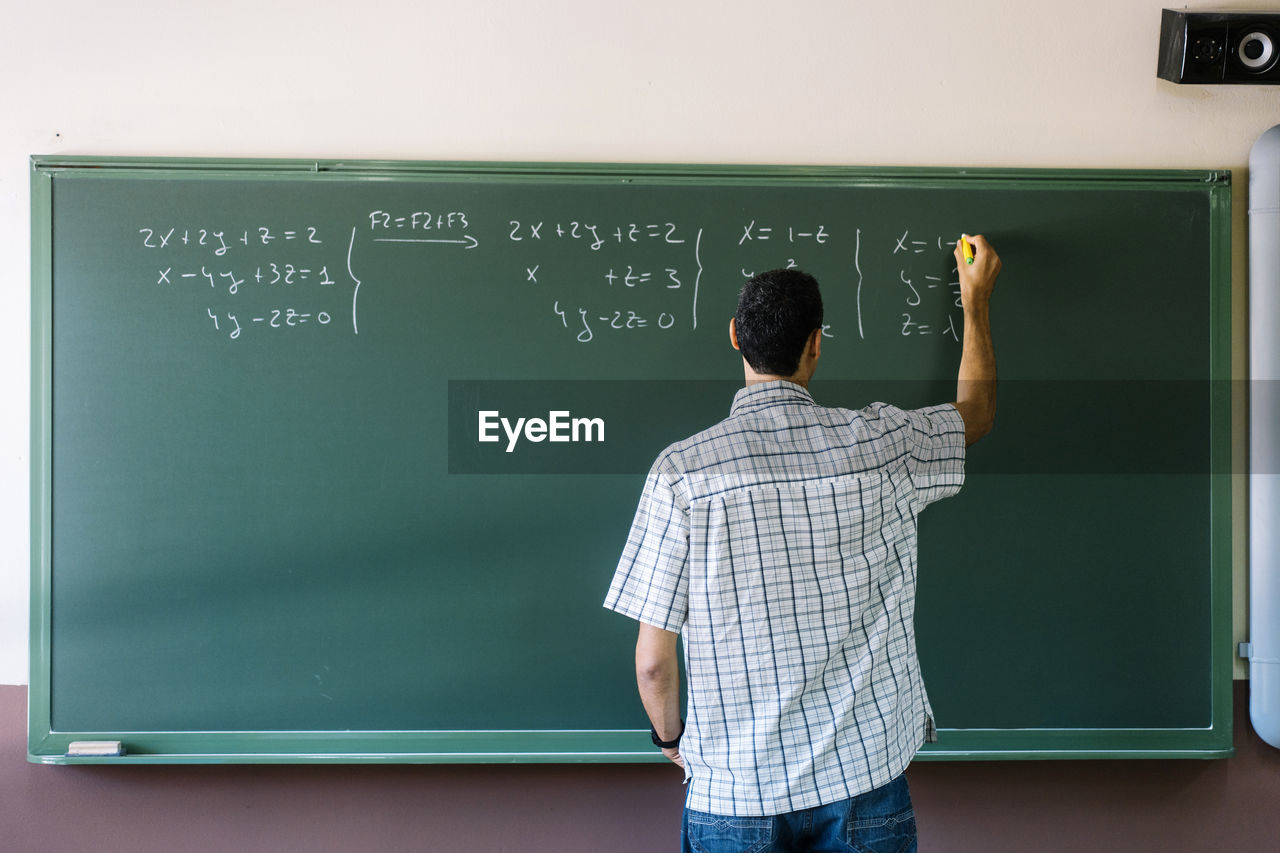 Math teacher writing formulas on chalkboard in classroom