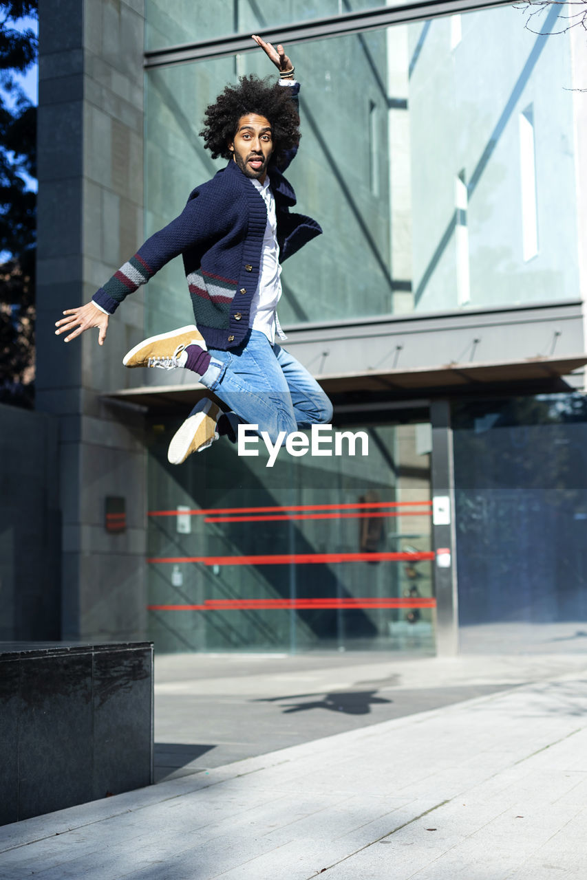 Full length portrait of young man jumping against building