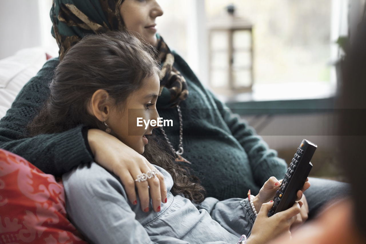 Daughter using remote control while sitting with mother at home