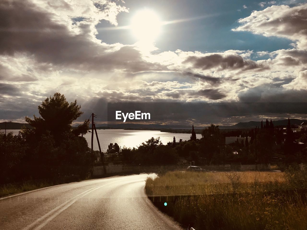 Road by trees against sky during sunset