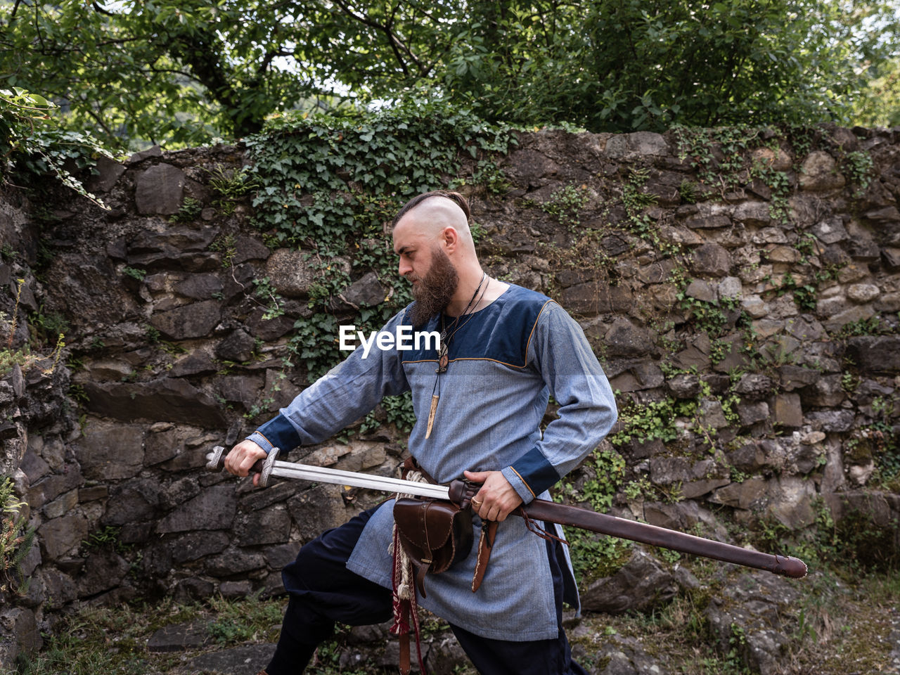 FULL LENGTH OF MAN HOLDING UMBRELLA STANDING AGAINST TREES