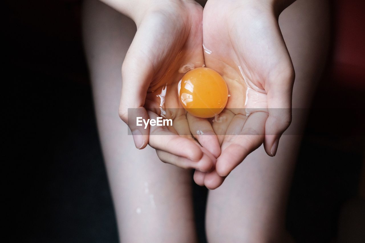 Midsection of naked woman holding egg yolk against black background