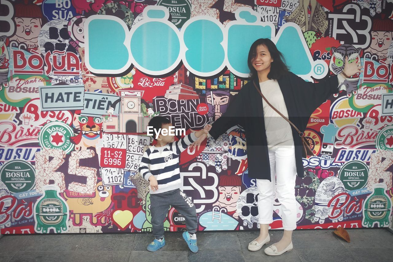 FULL LENGTH PORTRAIT OF YOUNG WOMAN STANDING AGAINST GRAFFITI