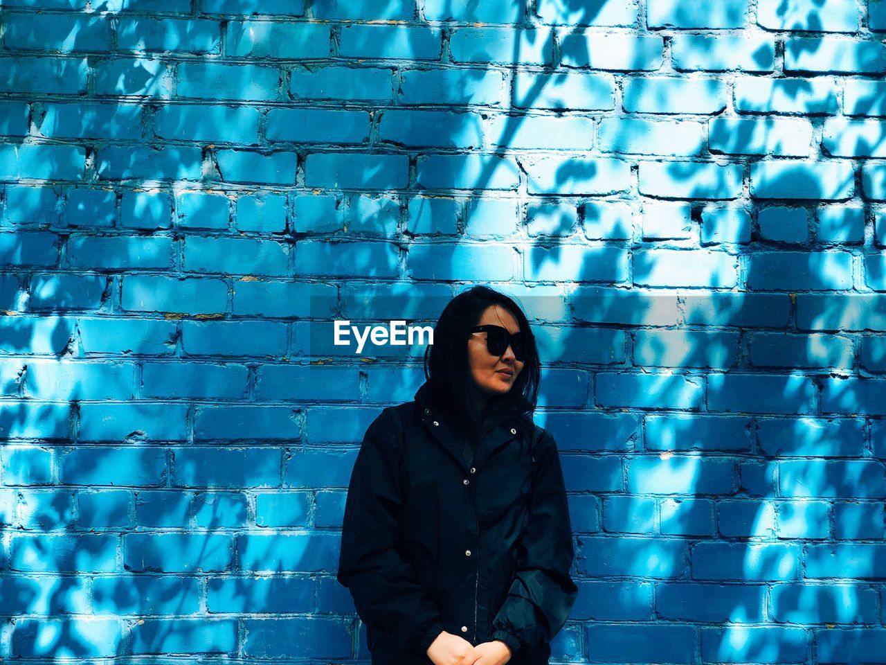 Woman wearing sunglasses standing against blue wall