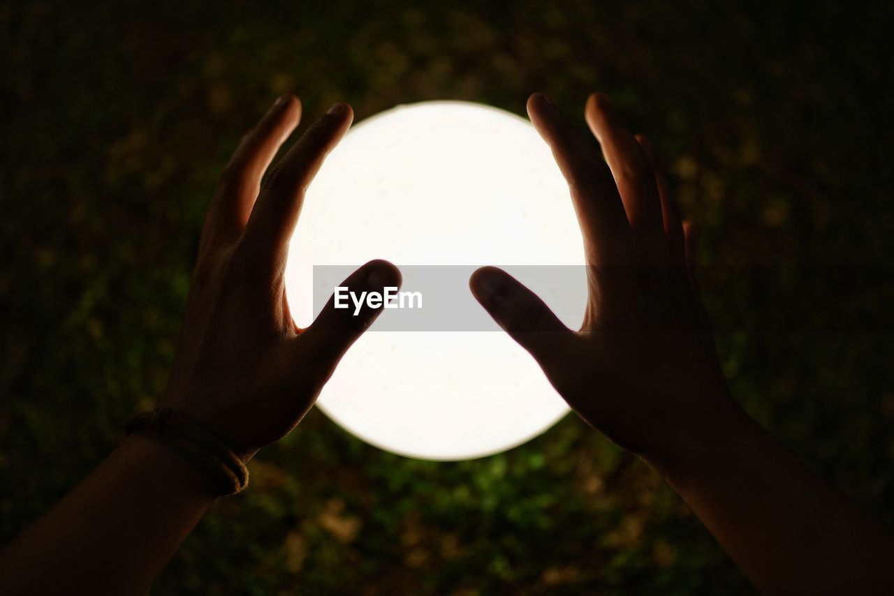 Optical illusion of cropped hands holding moon over field