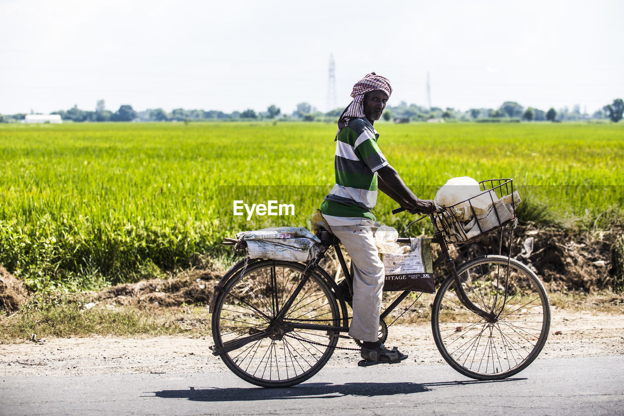 FULL LENGTH REAR VIEW OF MAN RIDING BICYCLE ON ROAD