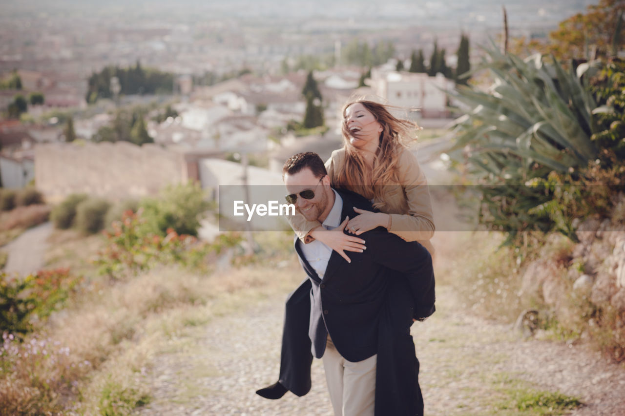 Man giving piggy back ride to happy woman standing on land