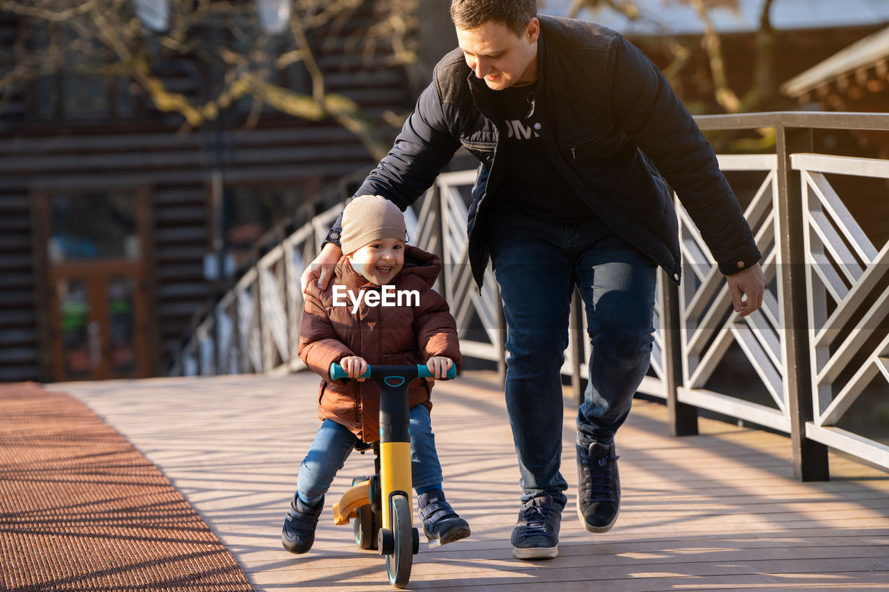 Happy father and son ride a bicycle on a bridge on a sunny day.