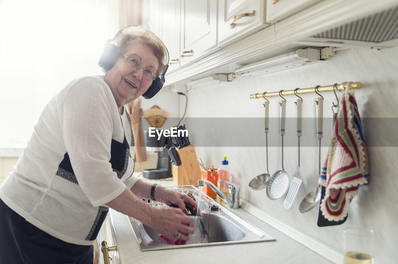 Portrait of senior woman listening music with headphones while washing up