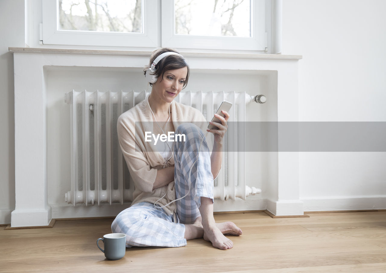 Woman at home sitting on floor with cell phone and headphones