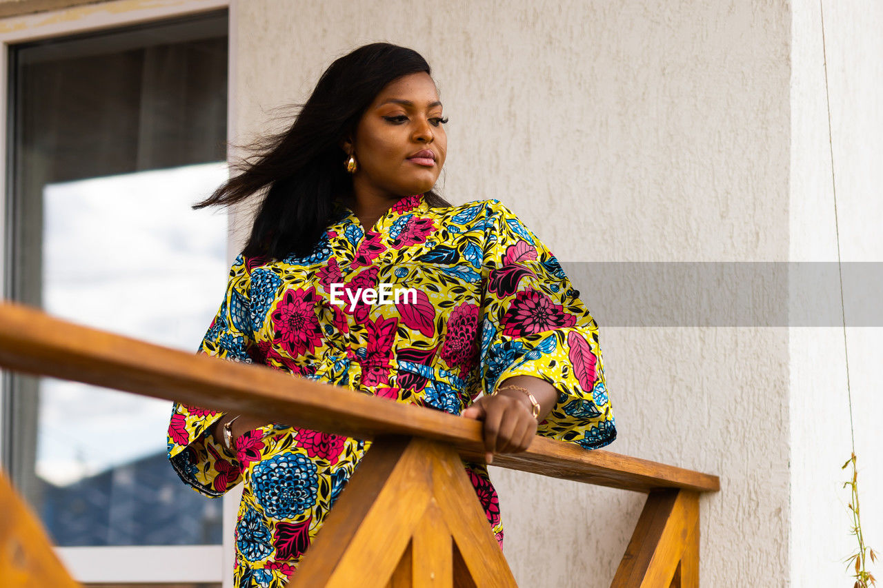 yellow, one person, women, adult, spring, architecture, standing, clothing, lifestyles, young adult, traditional clothing, hairstyle, female, dress, looking, portrait, person, building exterior, fashion, multi colored, photo shoot, outdoors, waist up, building, three quarter length, pattern, smiling, day, built structure, black hair, copy space, emotion, happiness, front view