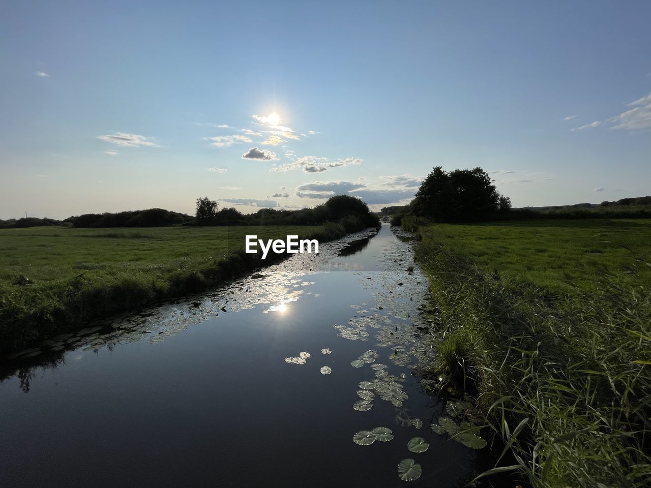 nature, sky, reflection, water, morning, environment, landscape, plant, horizon, land, sunlight, scenics - nature, grass, beauty in nature, cloud, river, dawn, no people, tranquility, field, rural scene, tree, wetland, marsh, tranquil scene, blue, outdoors, shore, coast, body of water, sun, non-urban scene, natural environment, rural area, summer, sunrise, travel, travel destinations, green