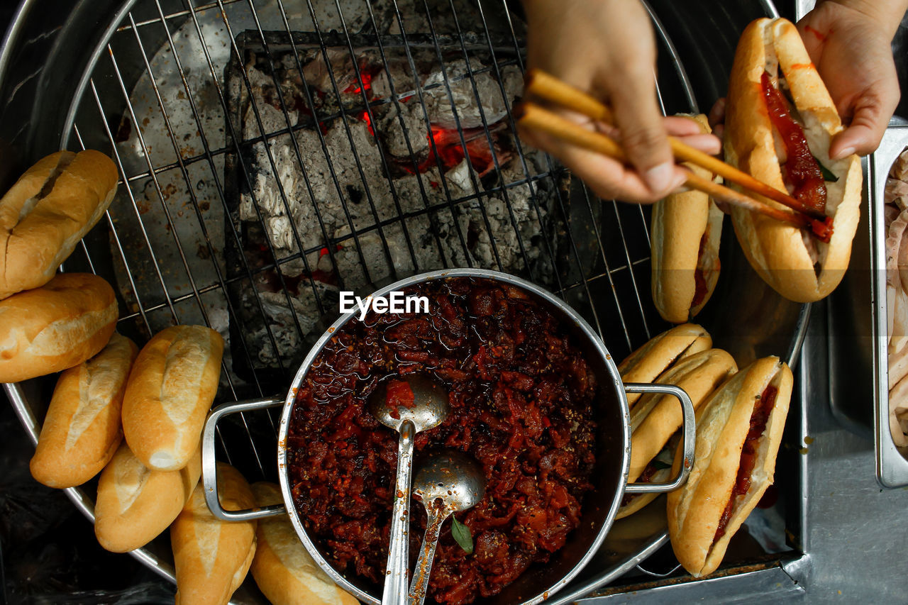 Directly above view of hands stuffing stewed pork into a banhmi in hue city night market, vietnam