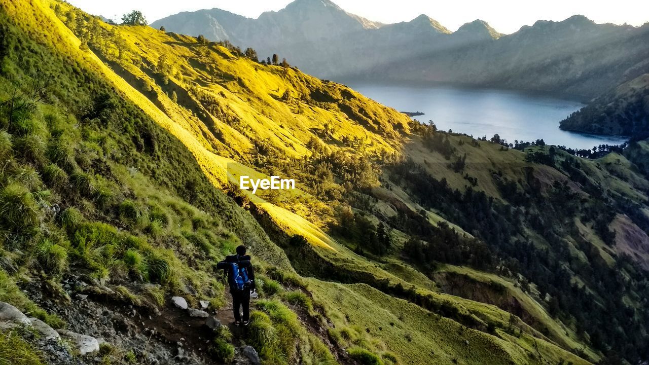 REAR VIEW OF MAN ON MOUNTAINS AGAINST SKY