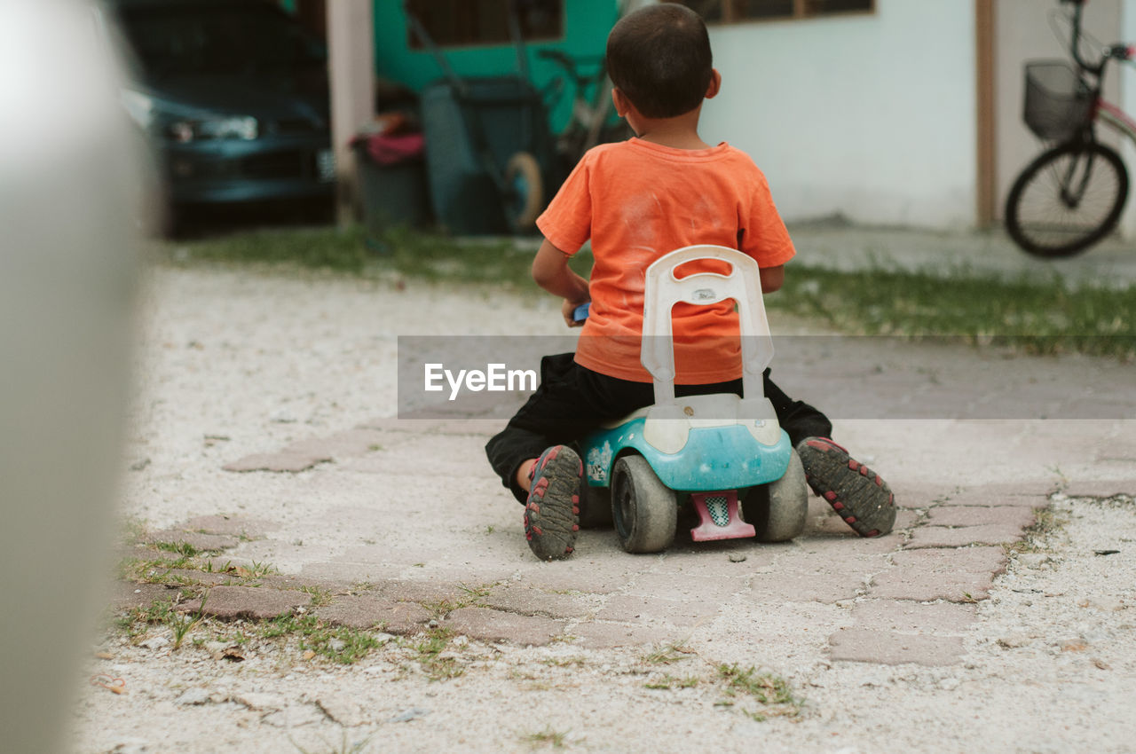 Rear view of boy playing with toy car on street