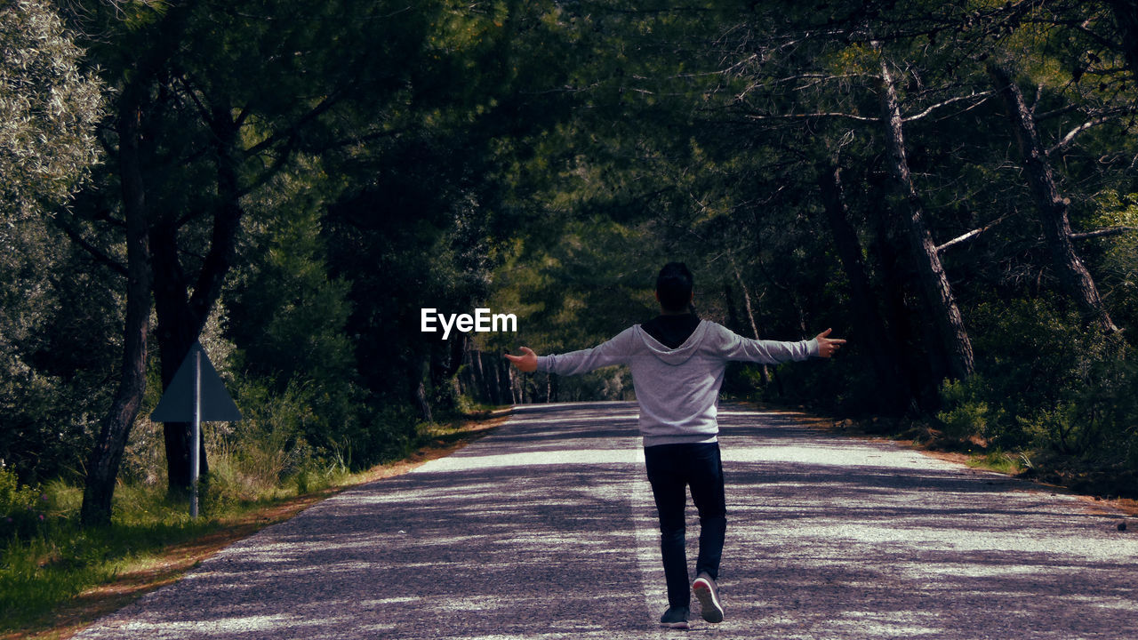 Rear view of young man with arms outstretched standing on road in forest