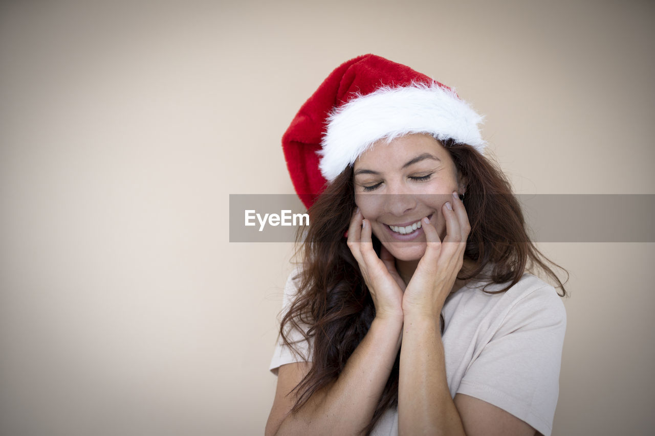 santa hat, christmas, happiness, hat, celebration, holiday, smiling, red, portrait, one person, emotion, women, adult, cheerful, studio shot, indoors, young adult, laughing, clothing, positive emotion, long hair, white, santa claus, costume hat, gift, fun, copy space, looking at camera, teeth, joy, headshot, female, smile, event, hairstyle, decoration, enjoyment, human face, front view, costume, waist up, lifestyles, brown hair, looking, photo shoot, dressing up