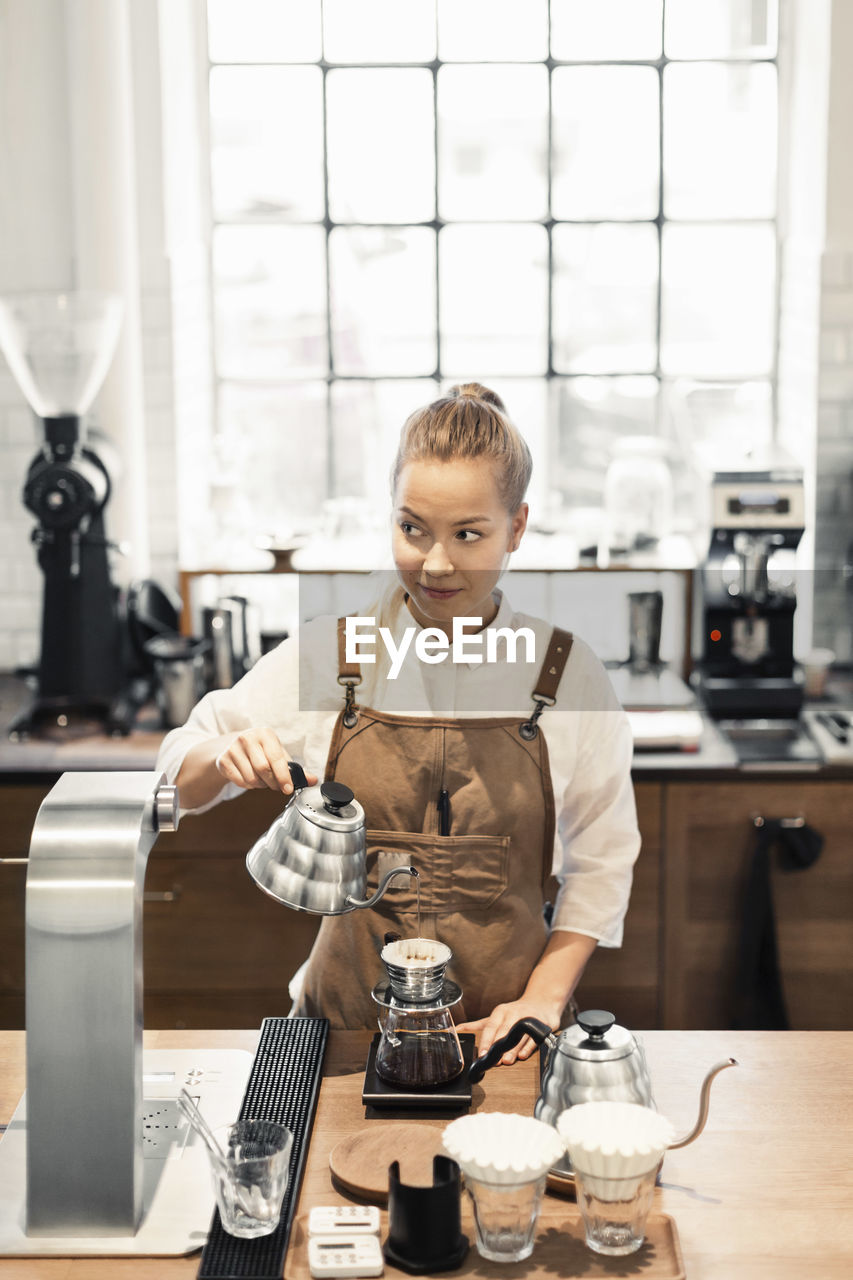 Female barista looking away while preparing coffee at cafe counter