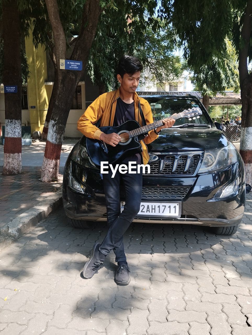 car, mode of transportation, transportation, motor vehicle, full length, one person, vehicle, adult, men, tree, casual clothing, city, musician, musical instrument, day, person, street, land vehicle, music, young adult, outdoors, arts culture and entertainment, guitar, musical equipment