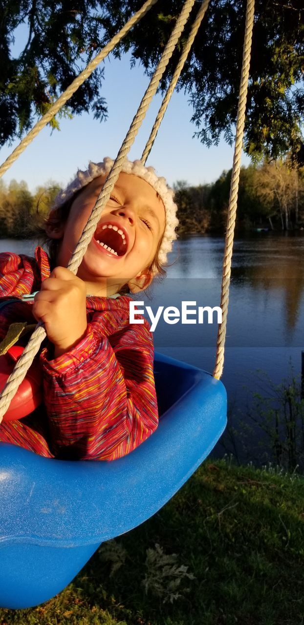 Cheerful girl swinging on rope swing against lake