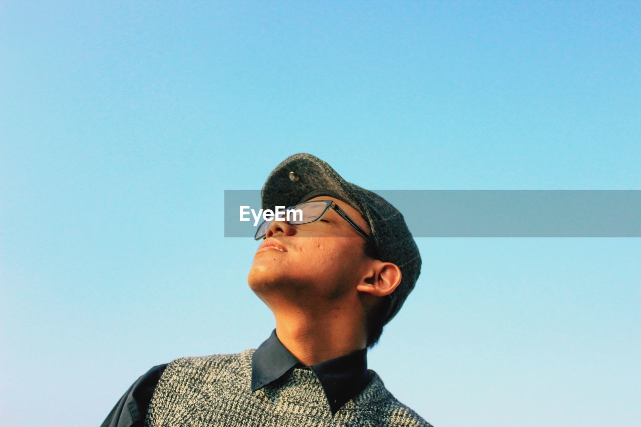 Low angle view of young man with eyes closed against blue sky