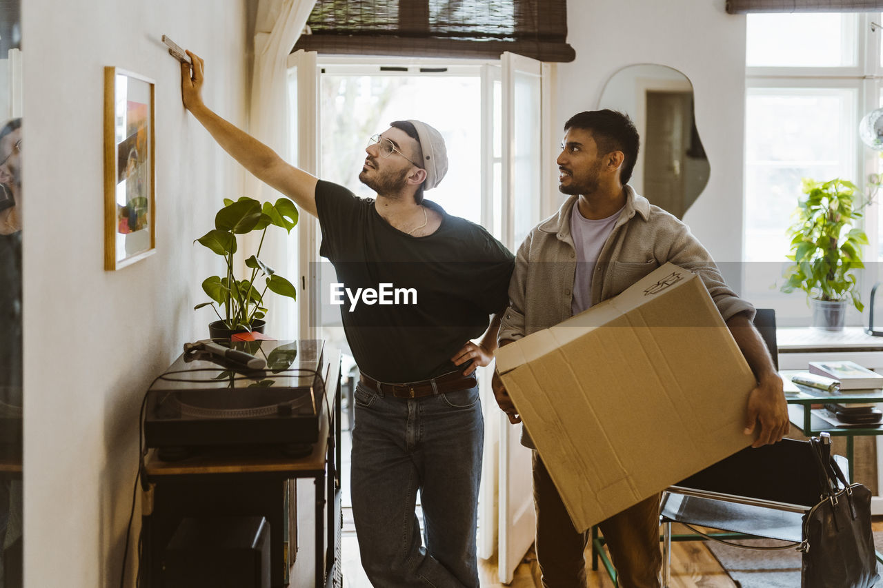 Man holding cardboard box while talking to boyfriend looking at painting on wall