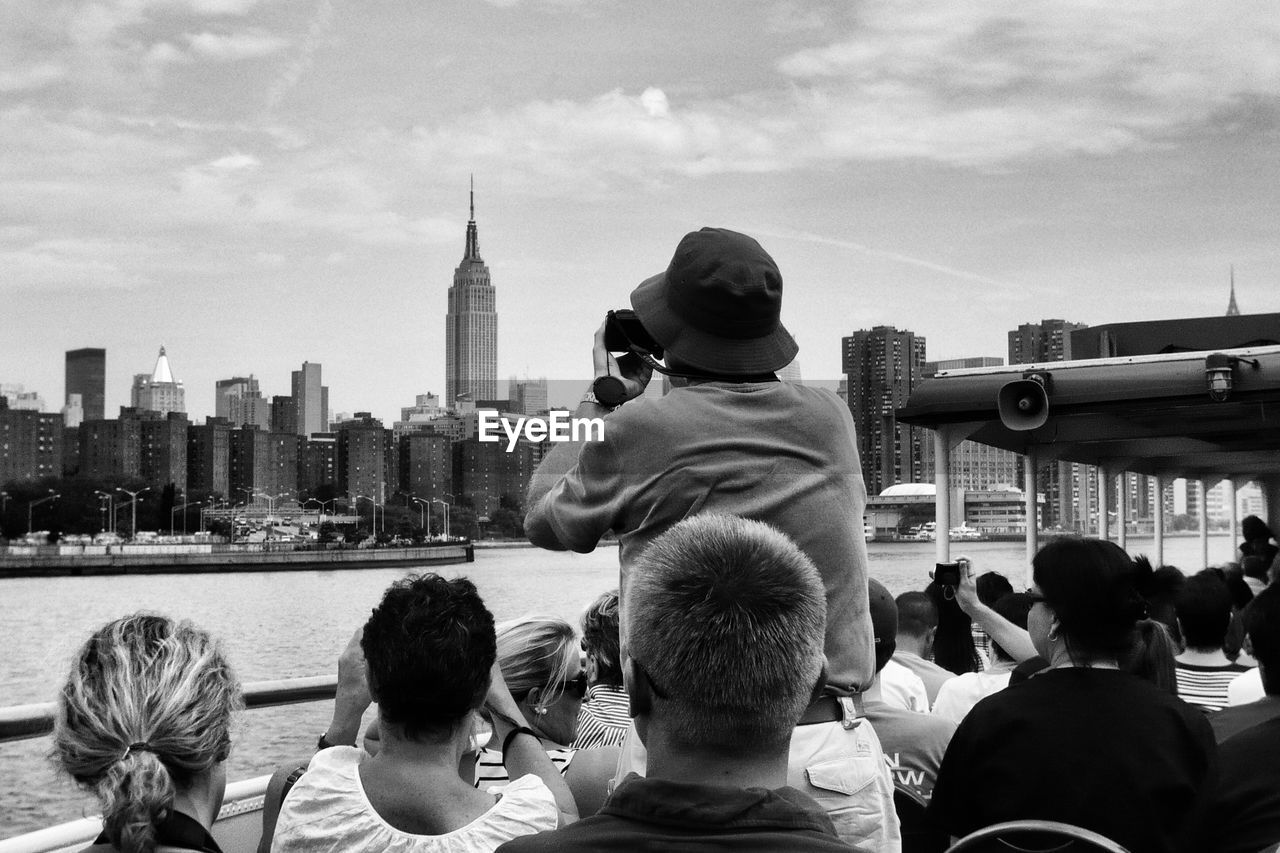 Tourist sailing on ferry by empire state building and city against sky