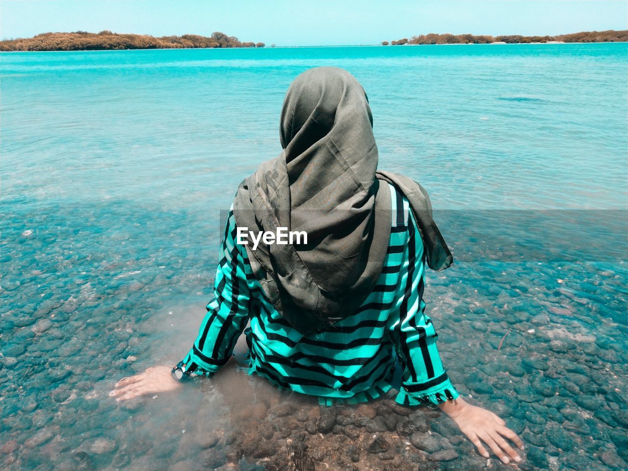 REAR VIEW OF MAN SITTING ON SHORE