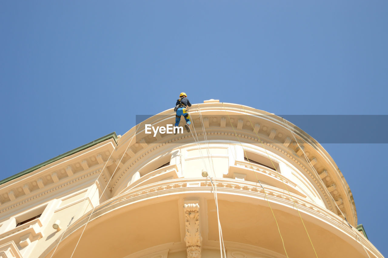 Low angle view of worker on rope while working at building