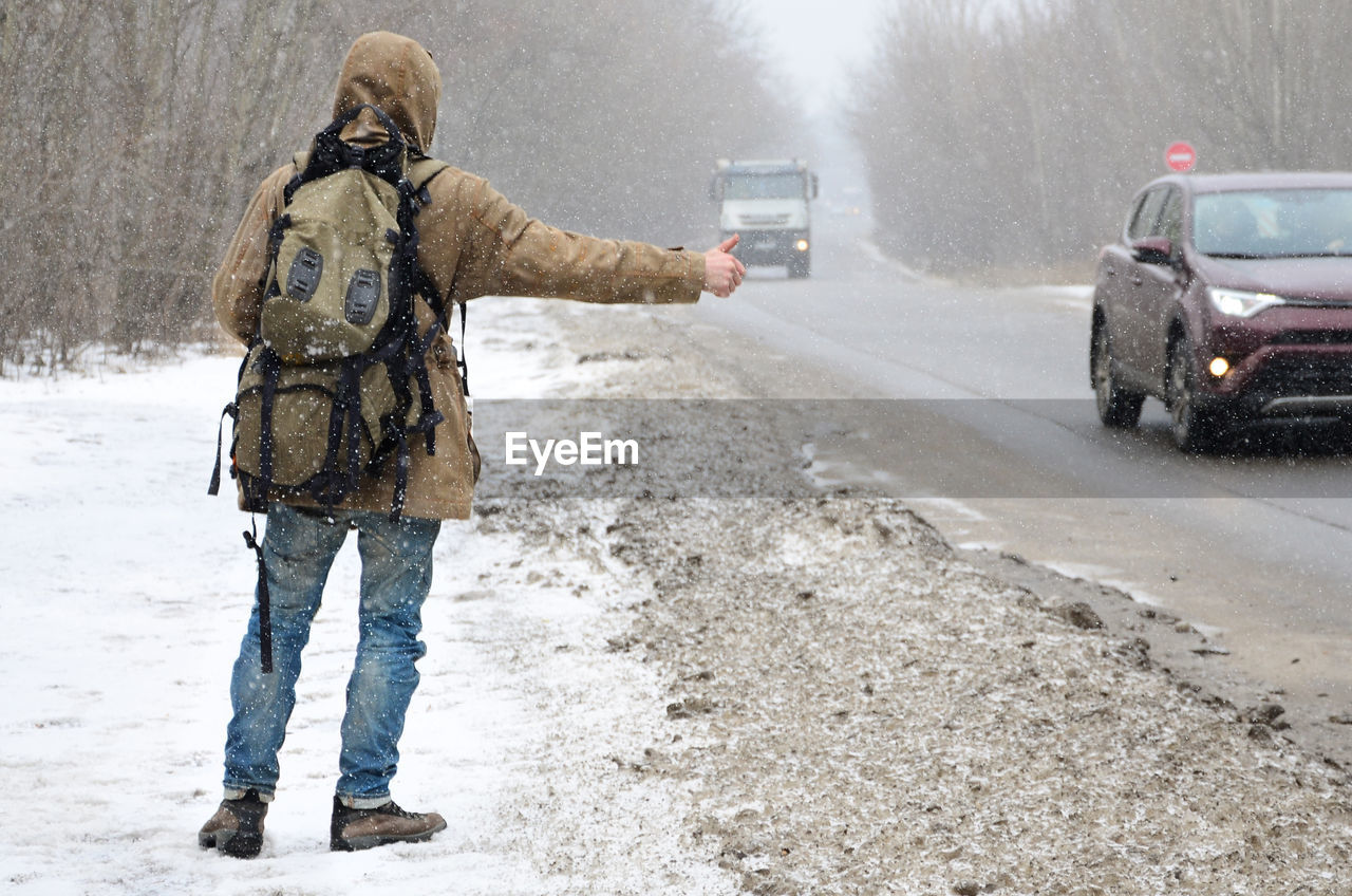 Rear view of man standing on snow by road