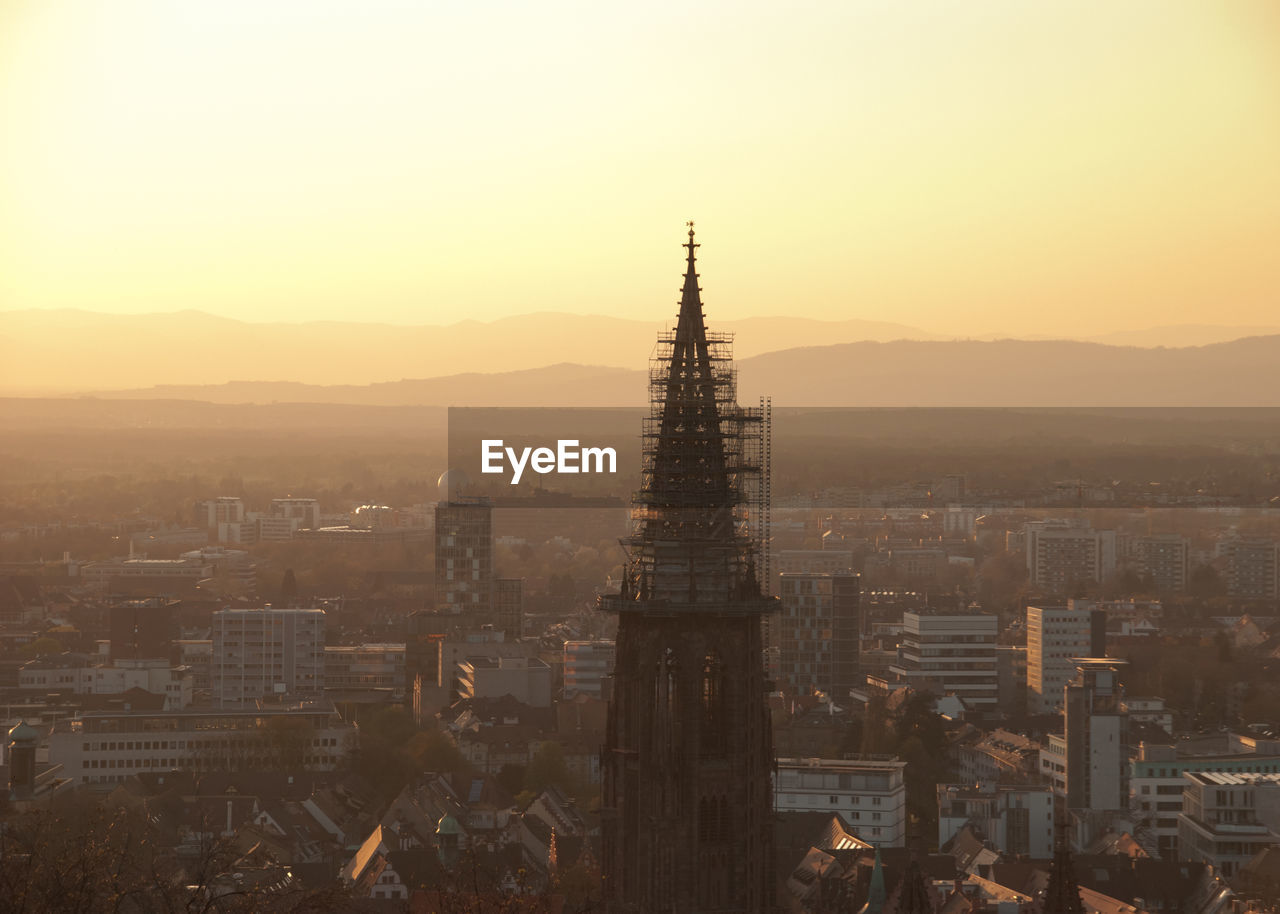 Freiburg minster and buildings in city against sky during sunset