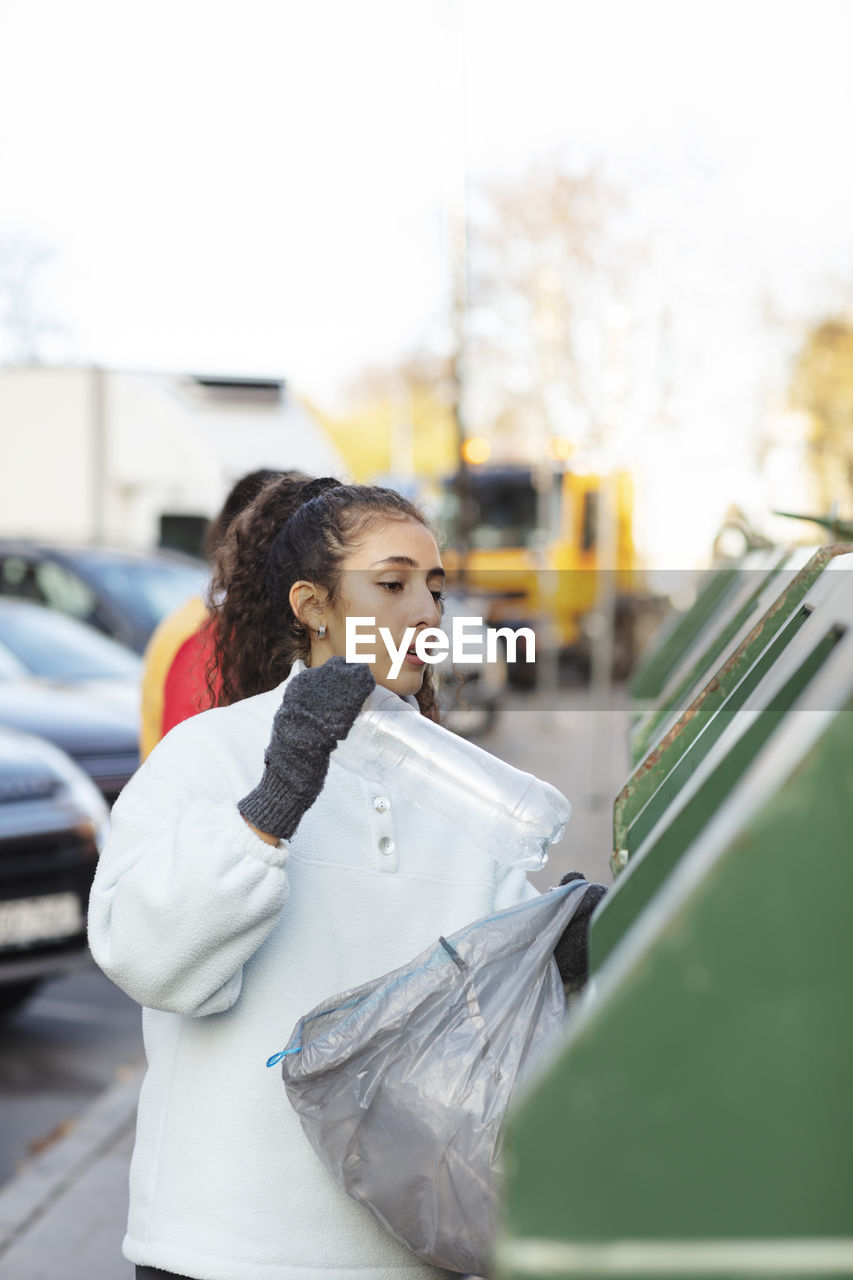 Female environmentalist throwing plastic bottle in garbage can