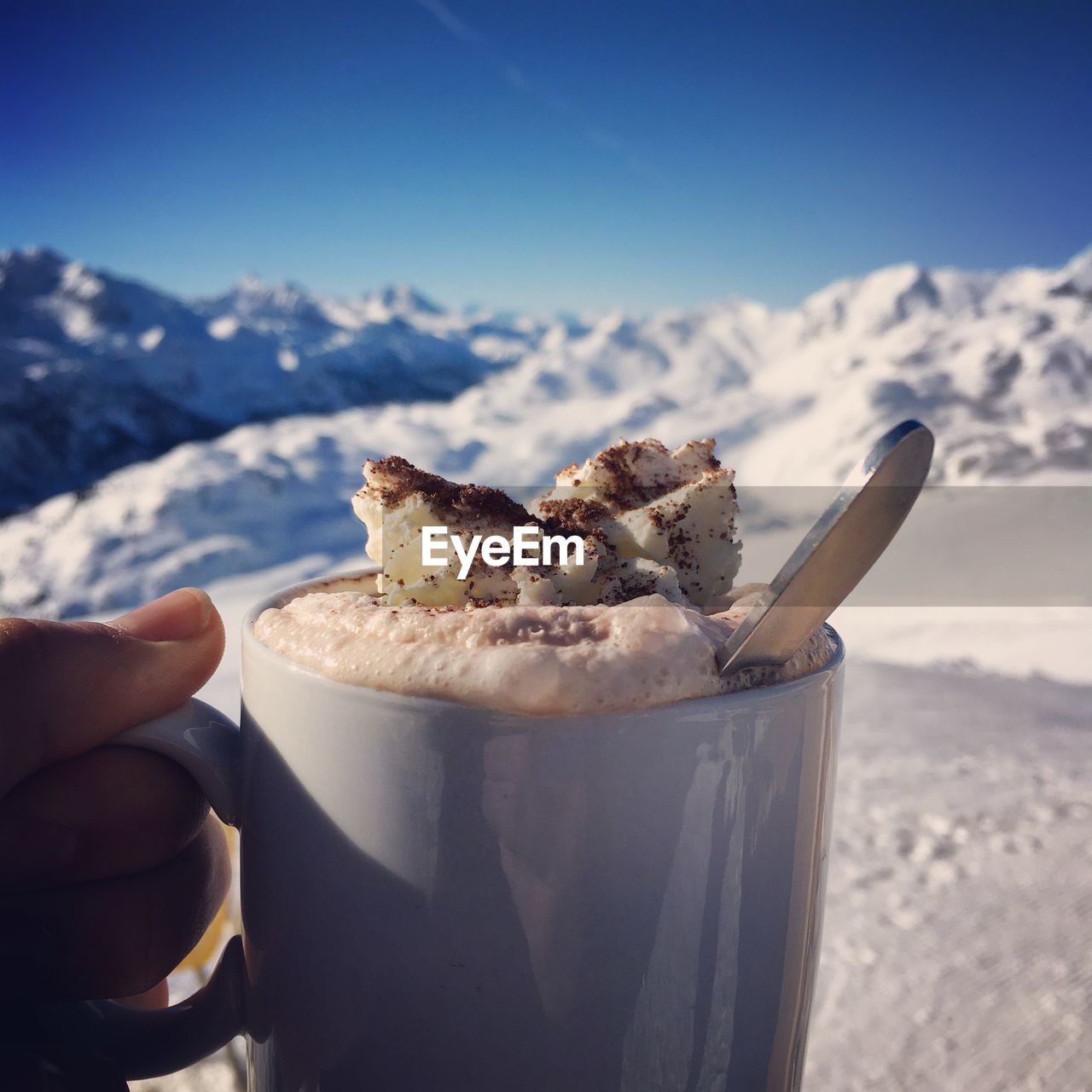 Close-up of hand holding coffee against snowy mountains