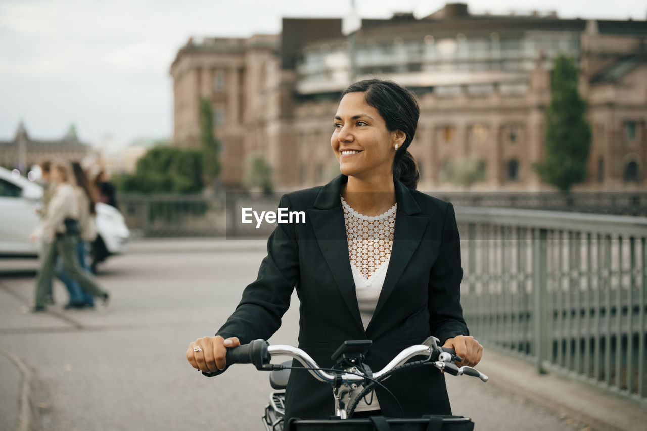 Smiling businesswoman with bicycle on bridge in city