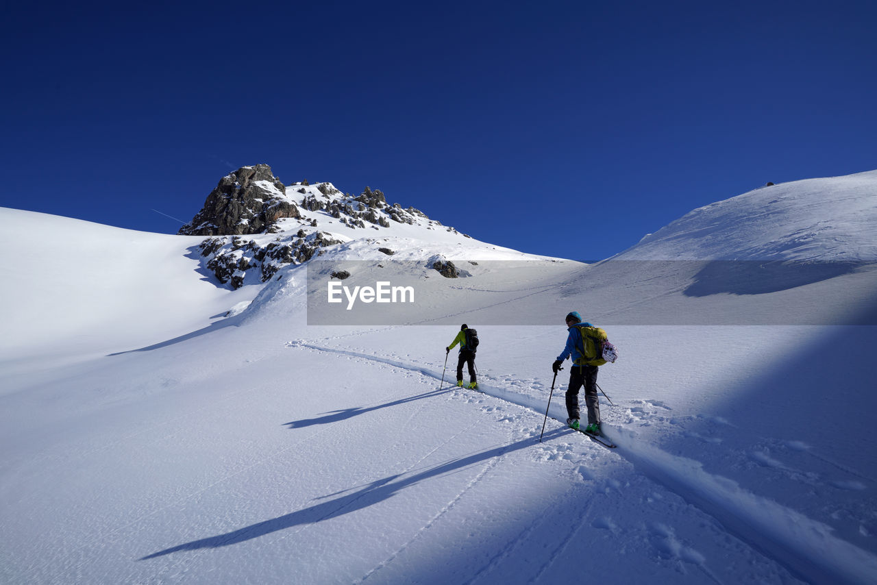 People skiing on snowcapped mountain against clear sky