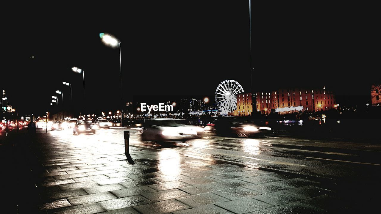 ILLUMINATED CITYSCAPE BY RIVER AGAINST SKY AT NIGHT