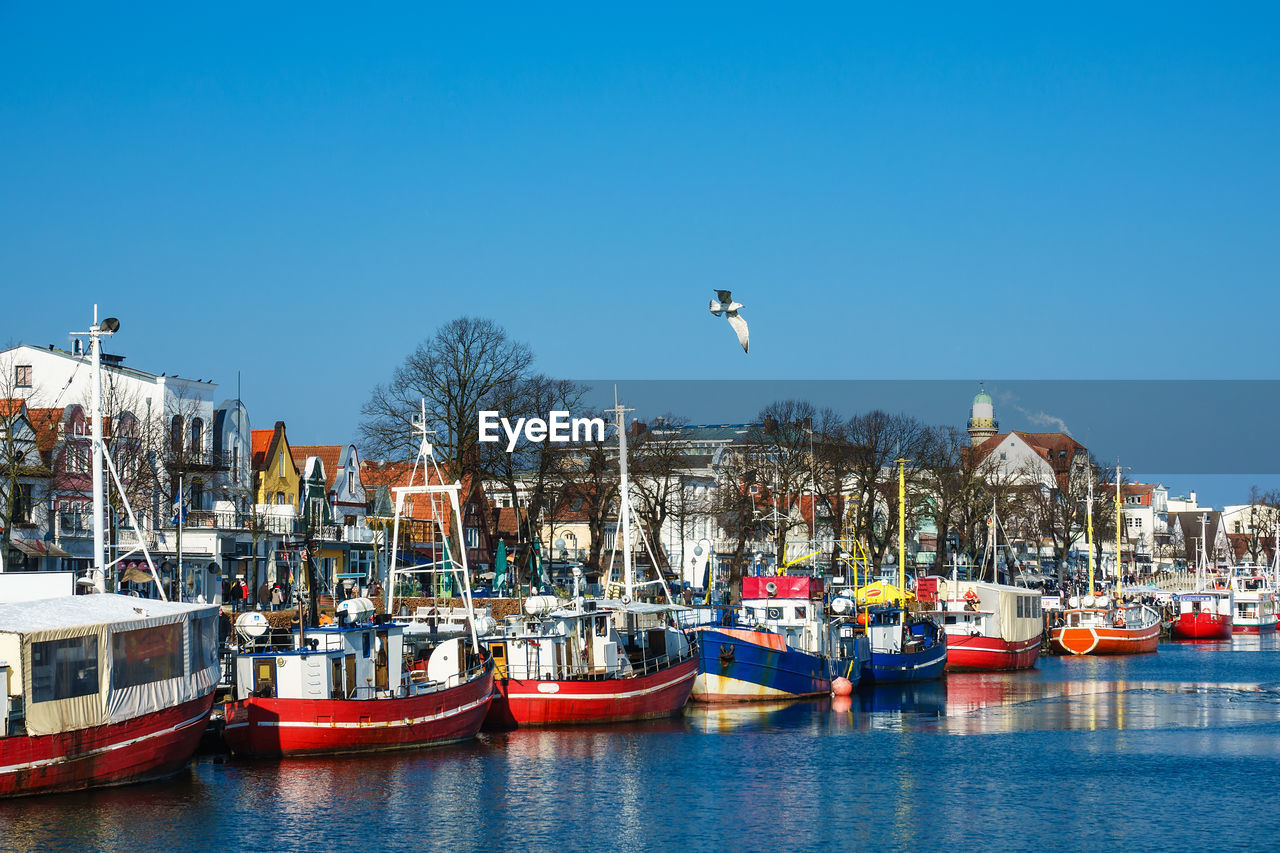 Boats moored at harbor against clear blue sky