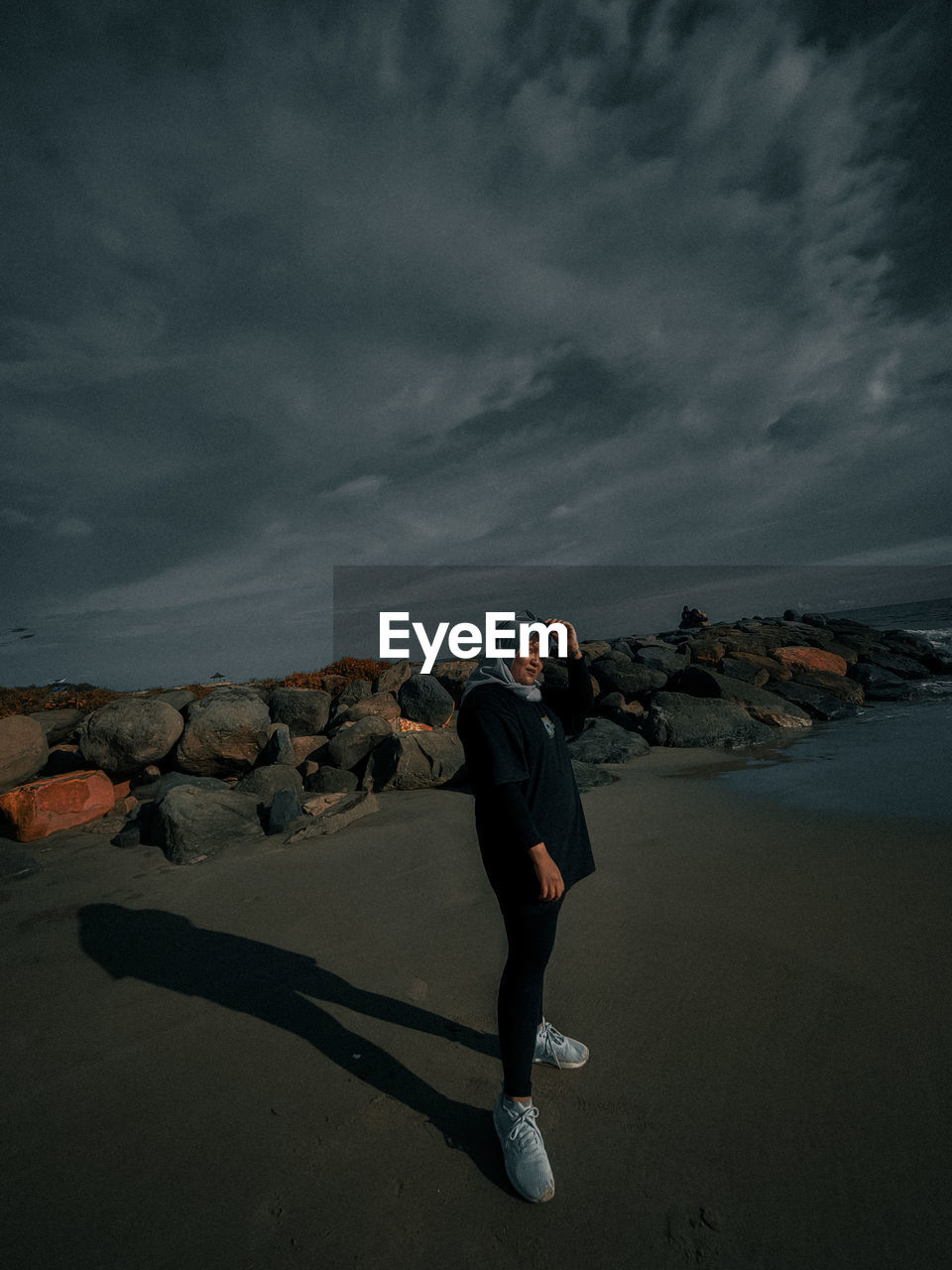 rear view of man walking on beach against sky during sunset