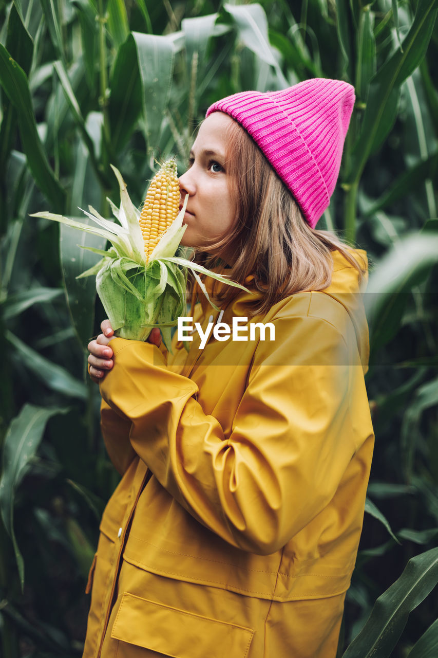 Funny little girl dressed in a yellow raincoat and a hot pink cap spoils and bites corn 