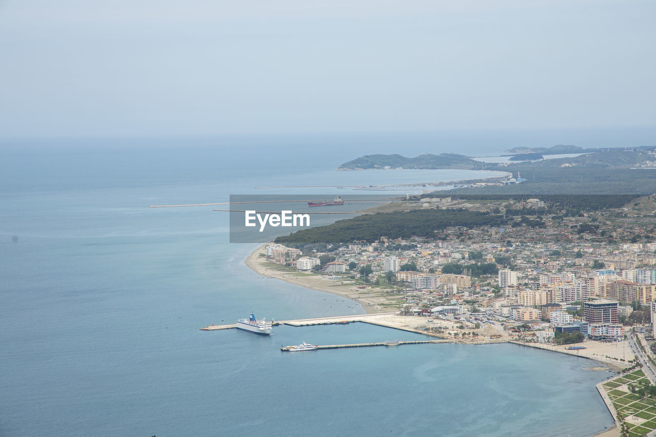 HIGH ANGLE VIEW OF CITY BY SEA AGAINST SKY