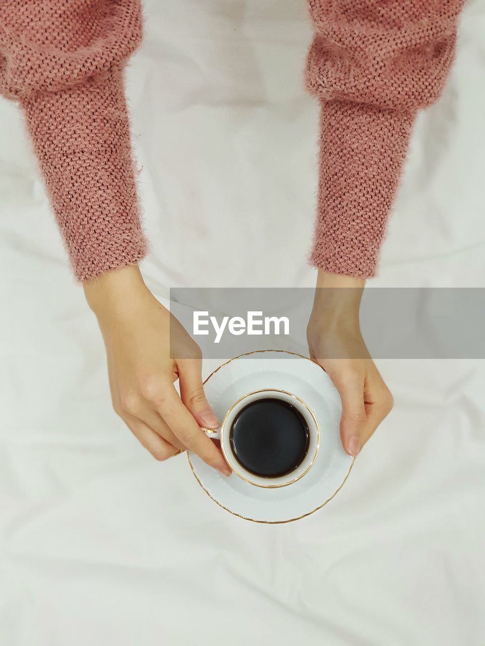 Cropped hands of woman holding coffee on bed