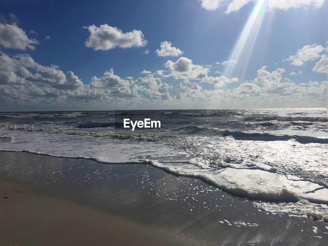 Scenic view of waves rushing towards shore against cloudy sky