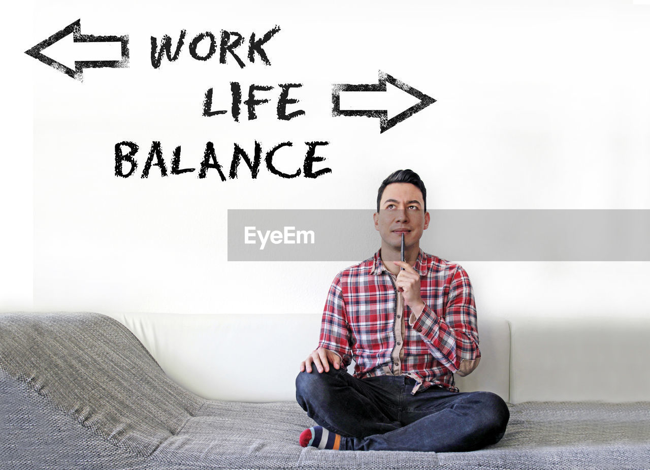The words work life balance on a wall, and a contemplating man sitting on a couch looking