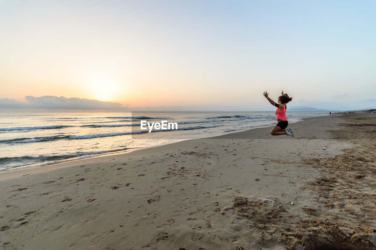 Side view of teenage girl jumping at beach during sunset