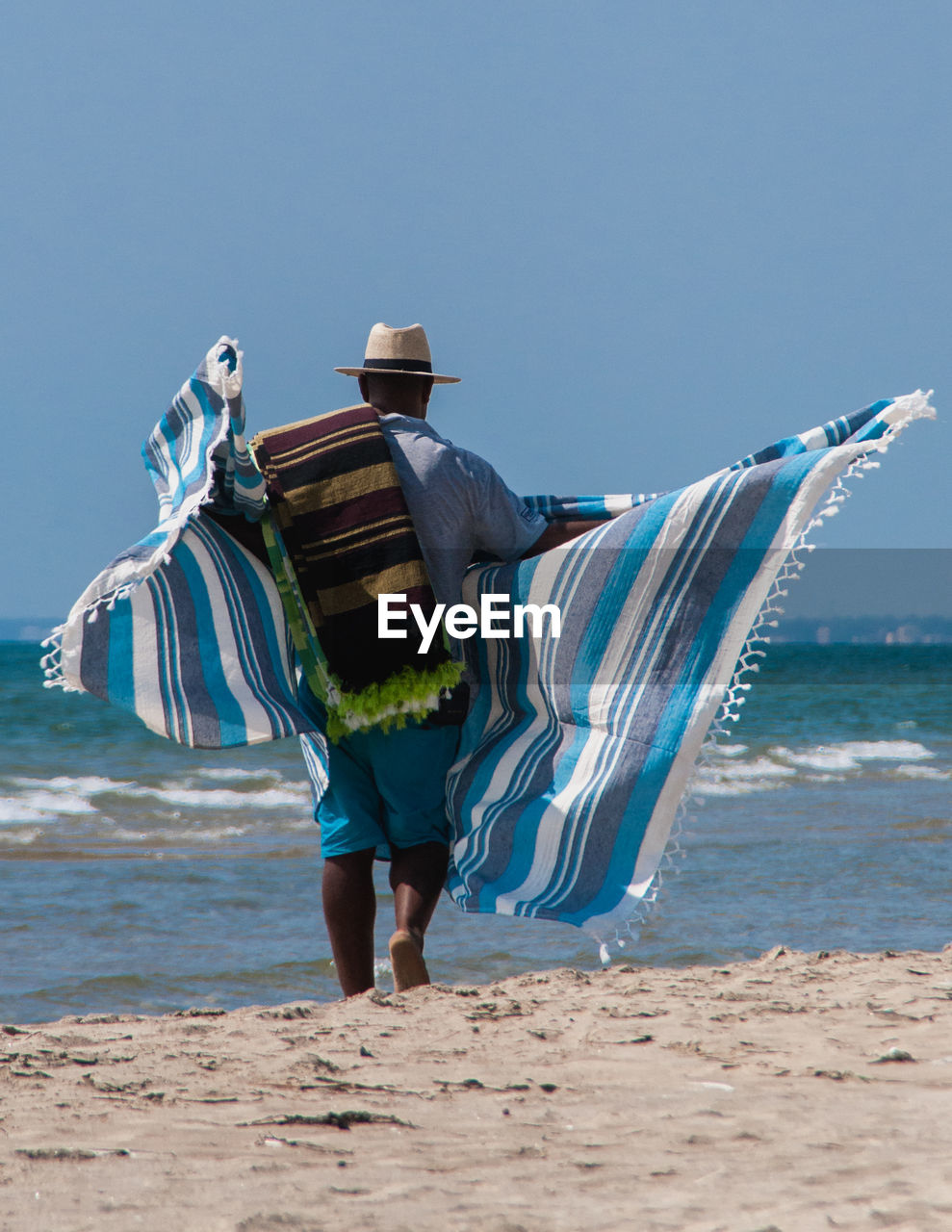 Rear view of man with sheet walking at beach against sky