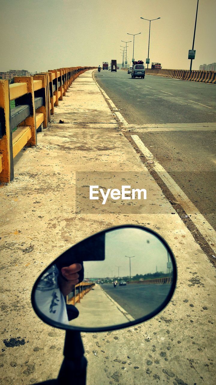 REFLECTION OF MAN PHOTOGRAPHING CAR ON ROAD